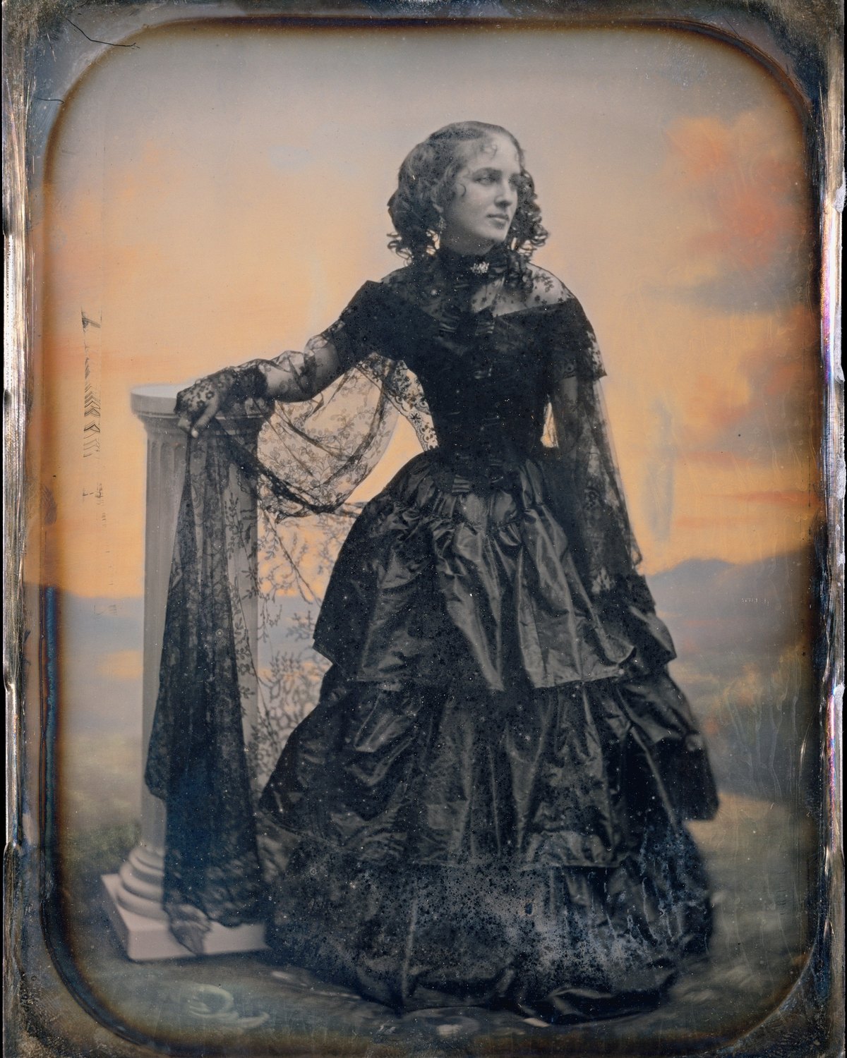 Dagherrotipo del 1850 circa: donna in abito di taffetà nero e scialle di pizzo, in piedi accanto a una colonna, espressione composta