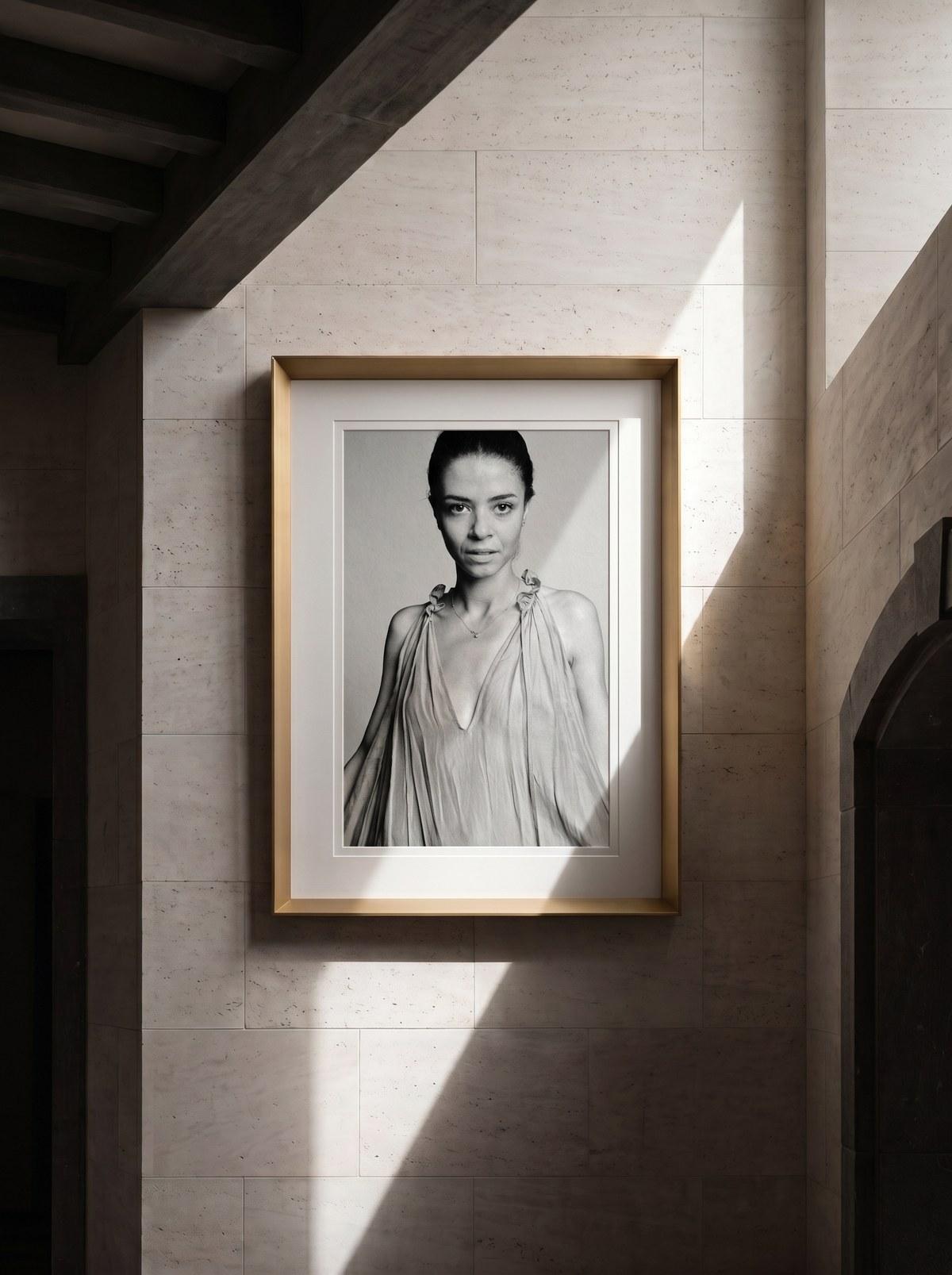 Ritratto Magneti® in cornice oro satinato appesa su parete in travertino, lama di luce naturale